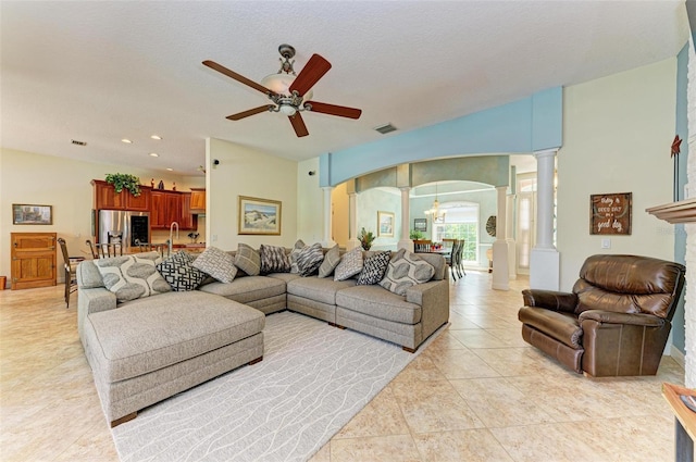 living room with ceiling fan with notable chandelier, a textured ceiling, light tile patterned floors, and decorative columns