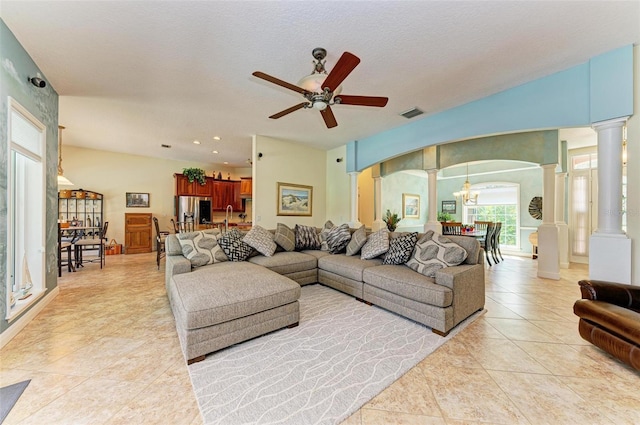 tiled living room with ceiling fan with notable chandelier, a textured ceiling, and ornate columns