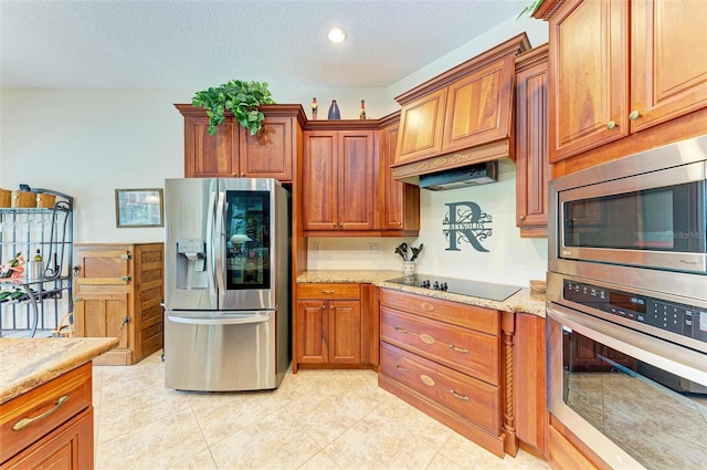 kitchen with a textured ceiling, custom range hood, appliances with stainless steel finishes, light stone counters, and light tile patterned flooring