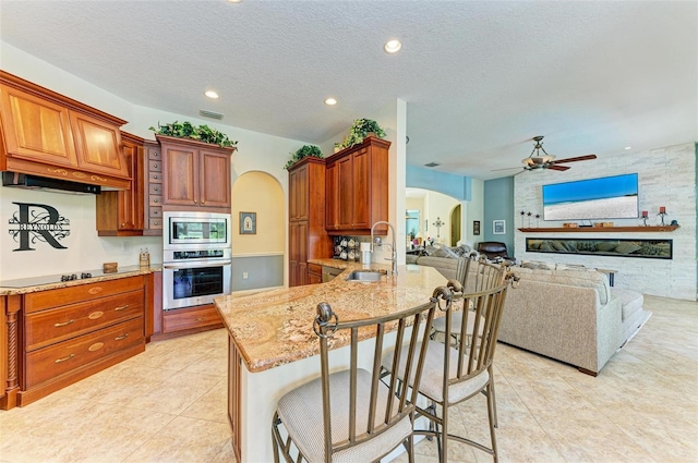 kitchen with light stone counters, stainless steel appliances, sink, ceiling fan, and a kitchen bar