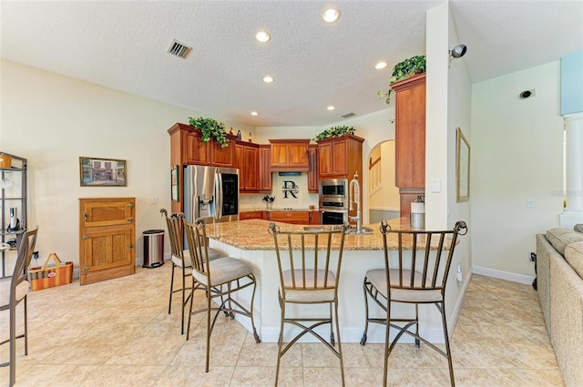 kitchen featuring a textured ceiling, a kitchen bar, stainless steel appliances, kitchen peninsula, and light stone countertops