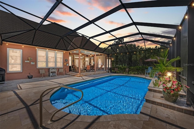 pool at dusk with glass enclosure and a patio