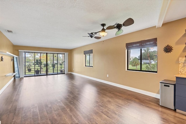 unfurnished room with a textured ceiling, ceiling fan, beam ceiling, and dark hardwood / wood-style flooring