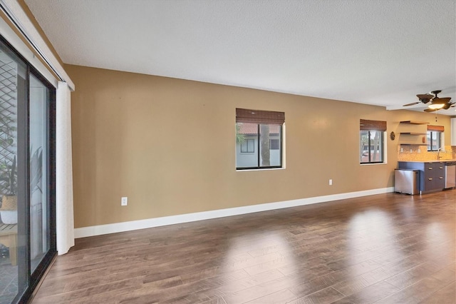 unfurnished living room featuring ceiling fan, dark hardwood / wood-style floors, sink, and a textured ceiling