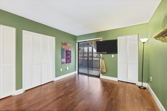 unfurnished bedroom featuring a textured ceiling, dark wood-type flooring, two closets, and access to exterior