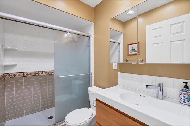 bathroom featuring a shower with shower door, toilet, vanity, and decorative backsplash