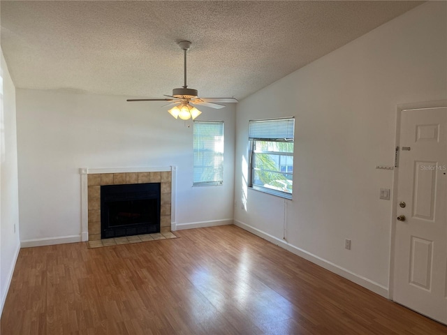 unfurnished living room with a textured ceiling, vaulted ceiling, ceiling fan, a tile fireplace, and hardwood / wood-style flooring