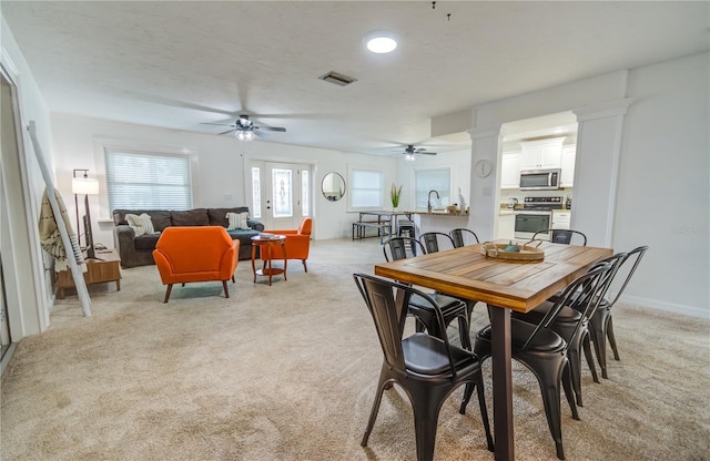 dining area featuring light colored carpet, ceiling fan, sink, and ornate columns