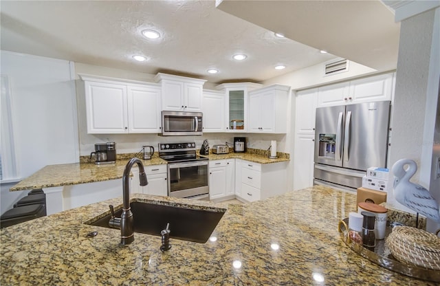 kitchen featuring appliances with stainless steel finishes, white cabinets, kitchen peninsula, sink, and stone counters