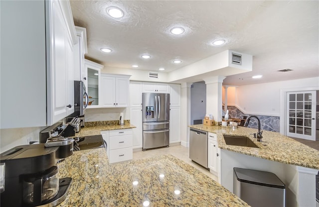 kitchen with appliances with stainless steel finishes, white cabinetry, sink, decorative columns, and a textured ceiling