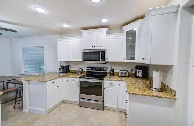 kitchen with appliances with stainless steel finishes, white cabinetry, kitchen peninsula, ceiling fan, and a kitchen bar