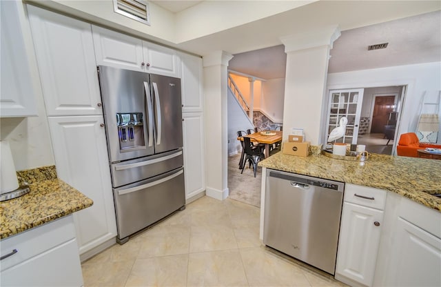 kitchen with stainless steel appliances, light stone counters, white cabinetry, and ornate columns