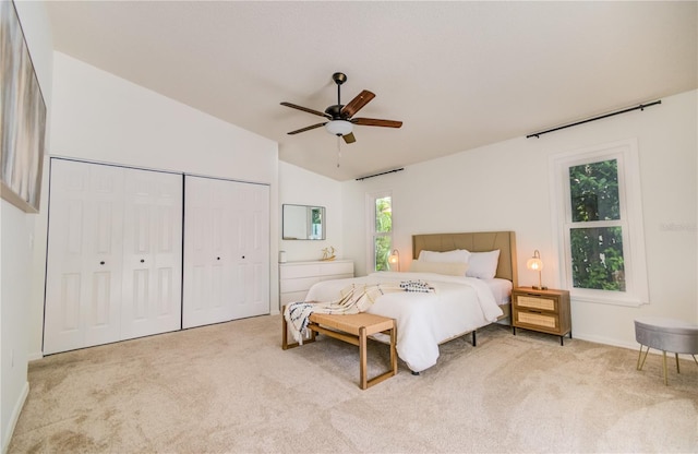 bedroom featuring lofted ceiling, two closets, ceiling fan, and light carpet