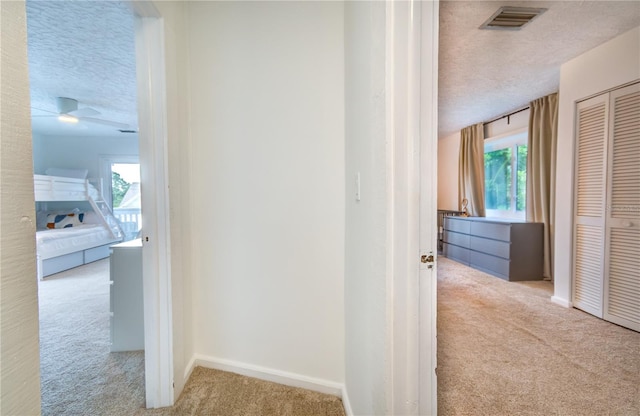 hall with light colored carpet and a textured ceiling