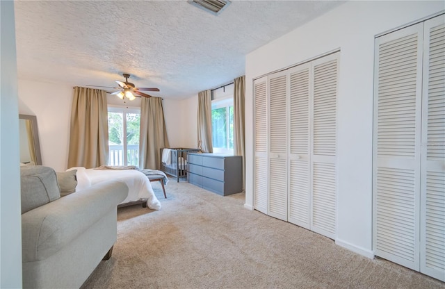 carpeted bedroom featuring ceiling fan, a textured ceiling, and multiple closets