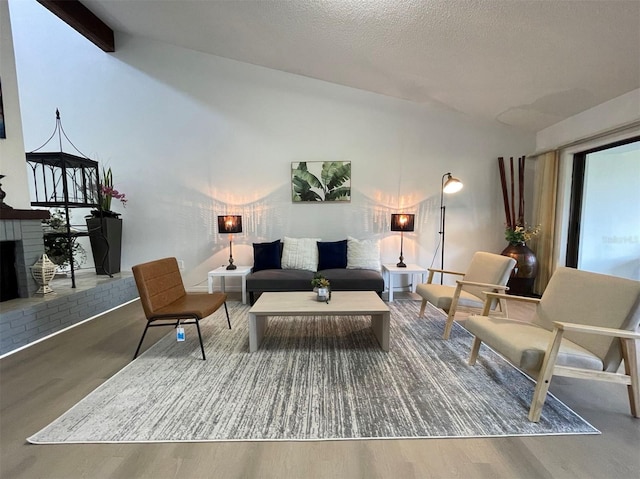 living room with vaulted ceiling with beams, a textured ceiling, hardwood / wood-style flooring, and a fireplace