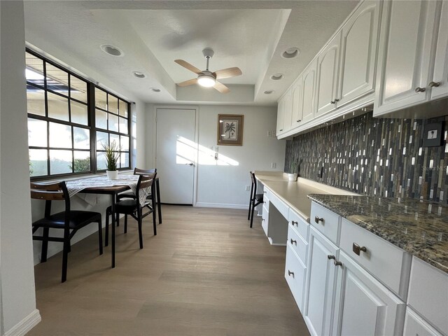 kitchen featuring white cabinets, a raised ceiling, backsplash, light wood-type flooring, and ceiling fan