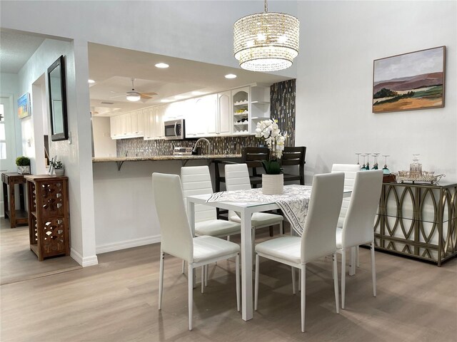 dining space with ceiling fan with notable chandelier, light wood-type flooring, and sink