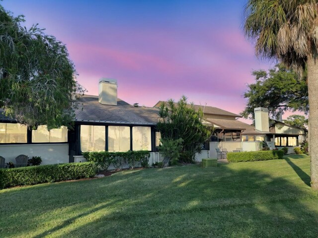 back house at dusk featuring a lawn