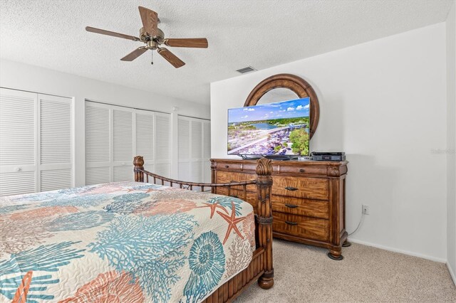 carpeted bedroom with multiple closets, ceiling fan, and a textured ceiling