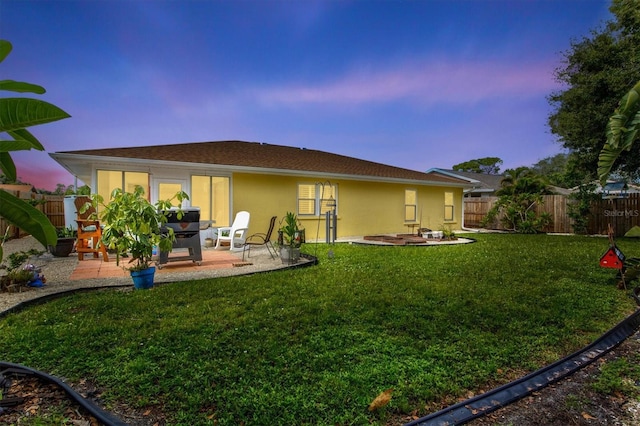 back house at dusk featuring a lawn and a patio