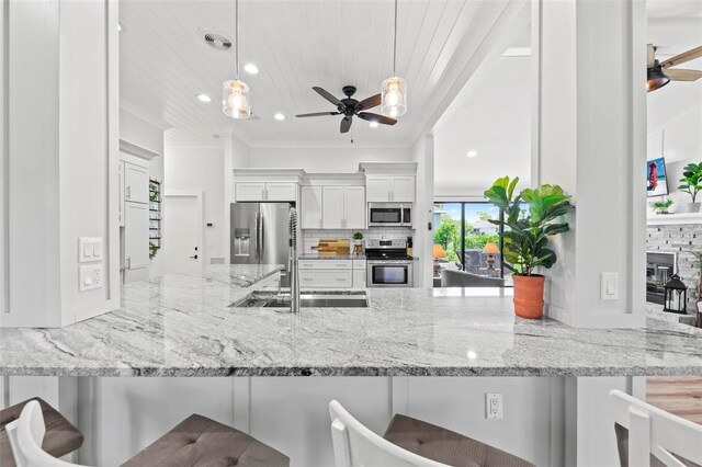 kitchen featuring decorative light fixtures, stainless steel appliances, white cabinetry, and a breakfast bar area