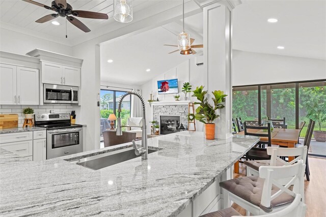 kitchen featuring light stone countertops, sink, vaulted ceiling, white cabinets, and appliances with stainless steel finishes