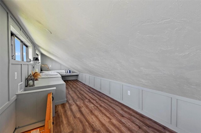 additional living space with a textured ceiling, lofted ceiling, and dark wood-type flooring