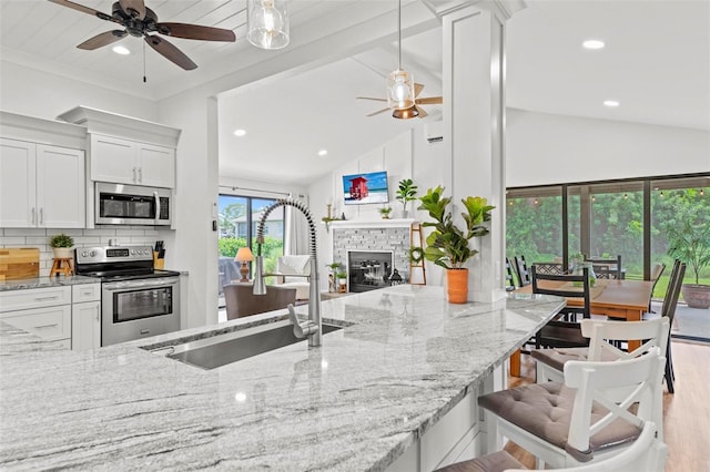 kitchen featuring appliances with stainless steel finishes, light stone counters, a sink, a ceiling fan, and decorative backsplash