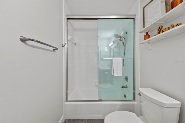 bathroom featuring toilet and bath / shower combo with glass door