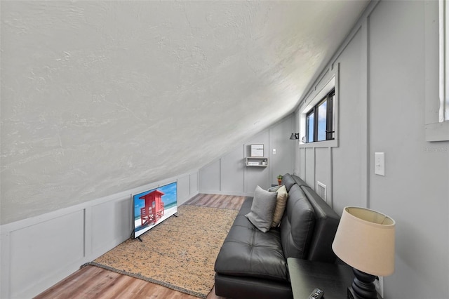 living area featuring a textured ceiling, vaulted ceiling, wood finished floors, and a decorative wall