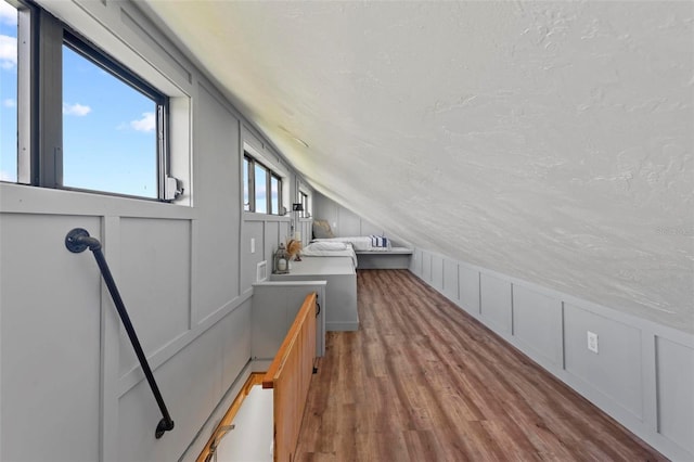 bonus room featuring wood finished floors, a textured ceiling, a decorative wall, and vaulted ceiling