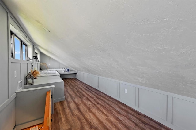 bonus room featuring vaulted ceiling, a textured ceiling, a decorative wall, and wood finished floors