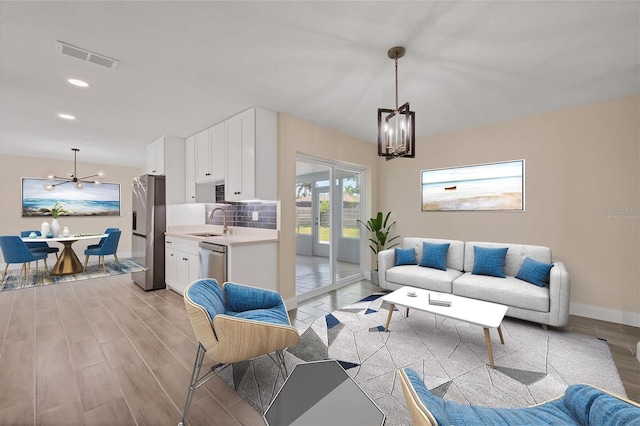 living room featuring sink, light hardwood / wood-style flooring, and a notable chandelier