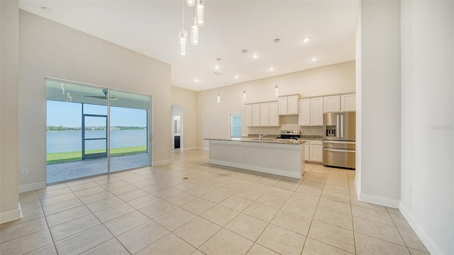 kitchen with stainless steel appliances, white cabinetry, a water view, an island with sink, and ceiling fan