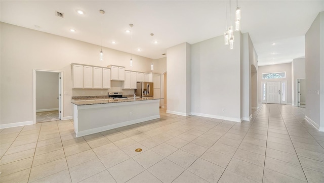 kitchen with stone counters, stainless steel appliances, white cabinetry, an island with sink, and pendant lighting