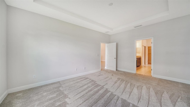 unfurnished bedroom featuring a raised ceiling, connected bathroom, and light colored carpet