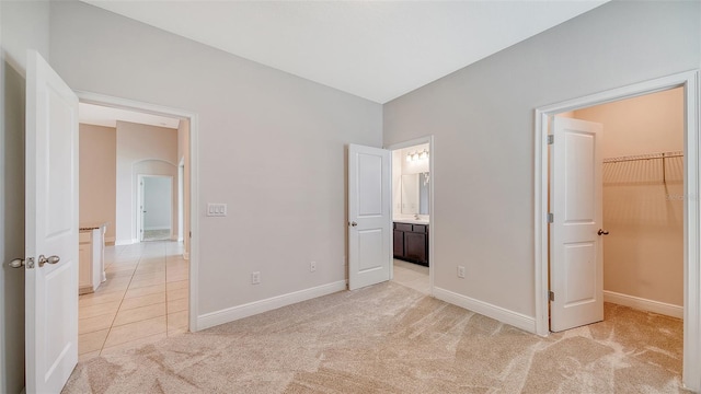 unfurnished bedroom featuring a closet, a spacious closet, ensuite bathroom, and light carpet