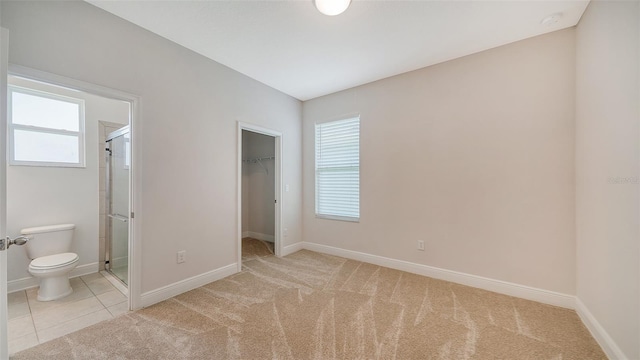 unfurnished bedroom featuring a closet, ensuite bath, light carpet, and a spacious closet