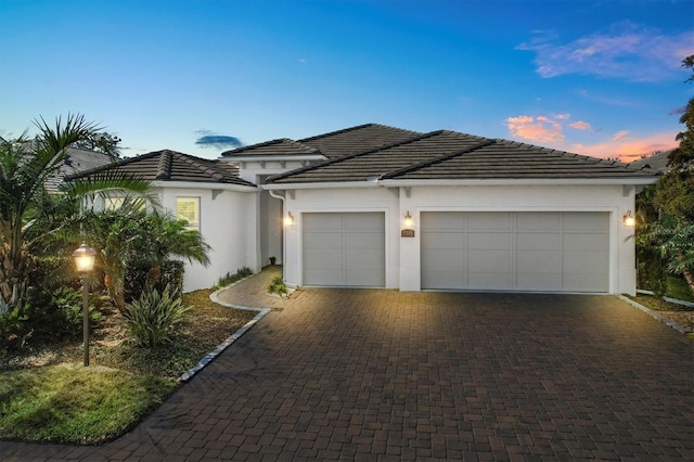 view of front of home featuring a tiled roof, decorative driveway, an attached garage, and stucco siding