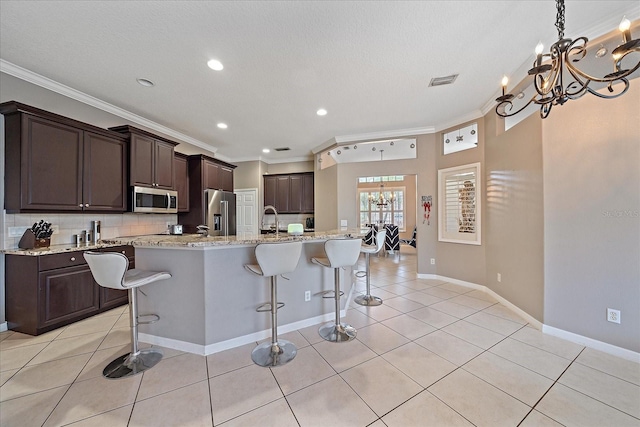 kitchen with appliances with stainless steel finishes, a notable chandelier, a kitchen bar, tasteful backsplash, and ornamental molding