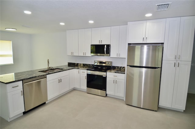 kitchen featuring sink, kitchen peninsula, dark stone countertops, white cabinetry, and stainless steel appliances