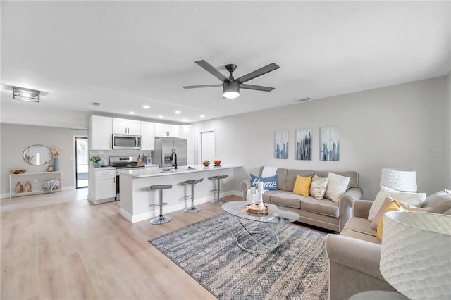 living room with a textured ceiling, light hardwood / wood-style flooring, ceiling fan, and sink