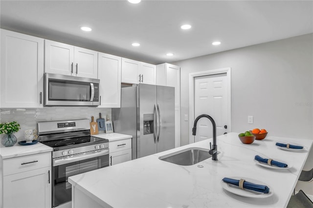 kitchen with appliances with stainless steel finishes, tasteful backsplash, sink, white cabinetry, and light stone counters