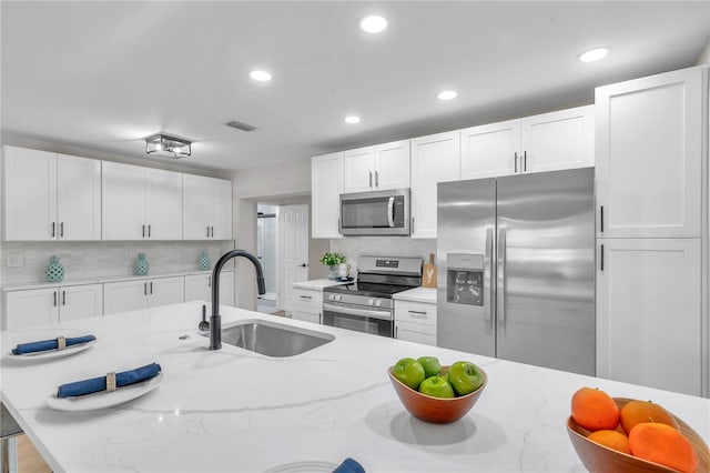 kitchen featuring appliances with stainless steel finishes, white cabinetry, sink, and light stone countertops