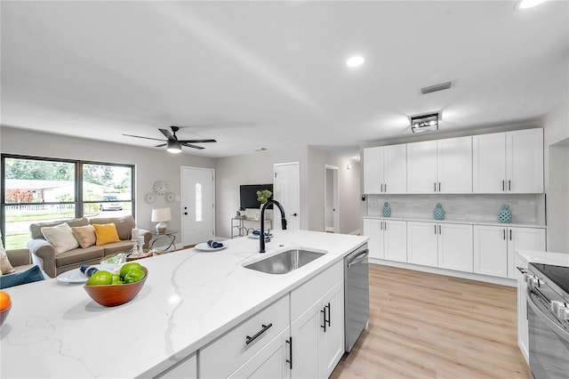 kitchen with light wood-type flooring, stainless steel appliances, sink, ceiling fan, and white cabinets