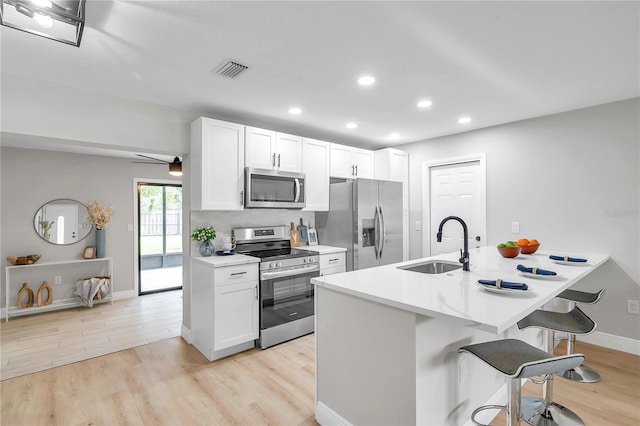 kitchen featuring white cabinets, stainless steel appliances, light hardwood / wood-style floors, sink, and a breakfast bar