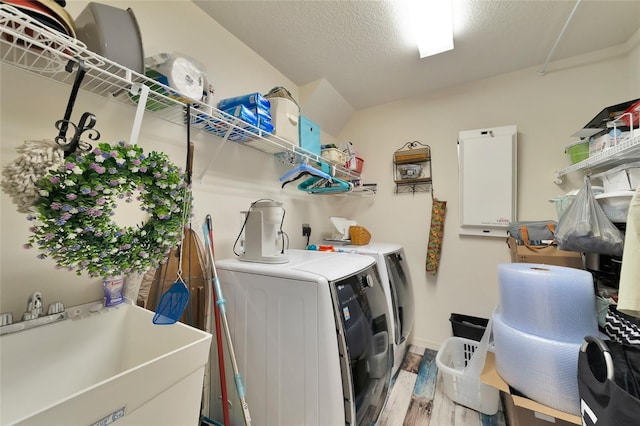 laundry area featuring a textured ceiling, independent washer and dryer, sink, and light hardwood / wood-style flooring