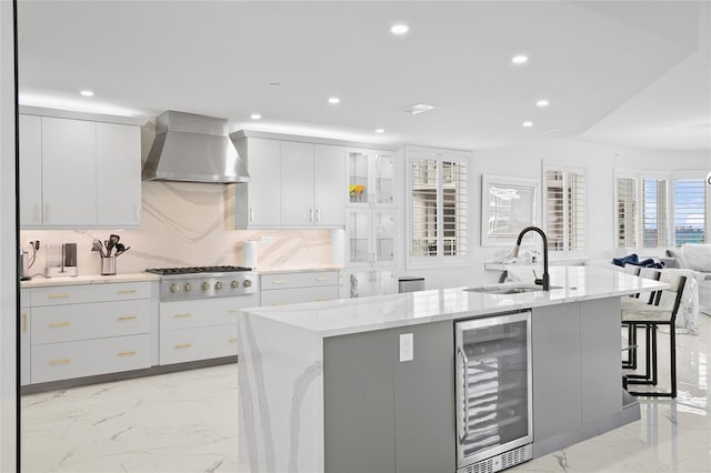 kitchen featuring stainless steel gas stovetop, marble finish floor, wine cooler, a sink, and wall chimney exhaust hood