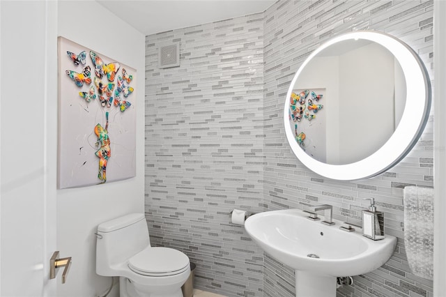 bathroom with backsplash, tile walls, toilet, and a sink